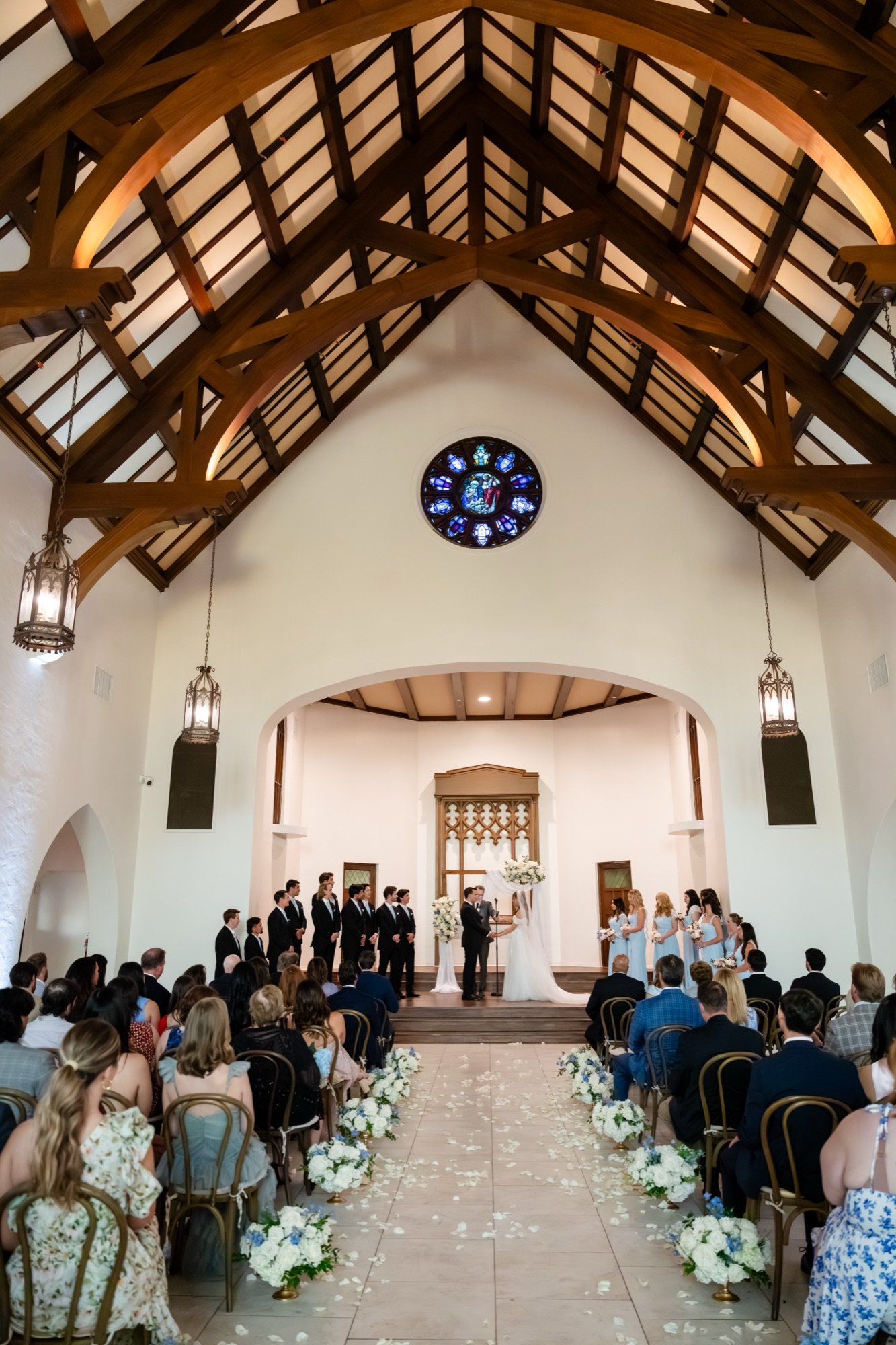 A ceremony at The Sanctuary in Long Beach, guests seated beneath dark wood ceiling trusses and a round stained glass window