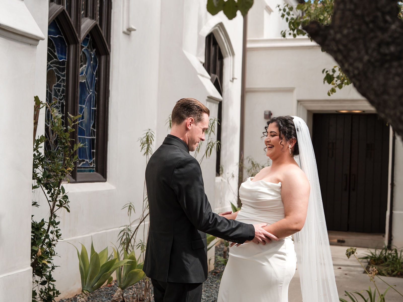 A bride and groom sharing a first look in the brick courtyard beside a stained glass window