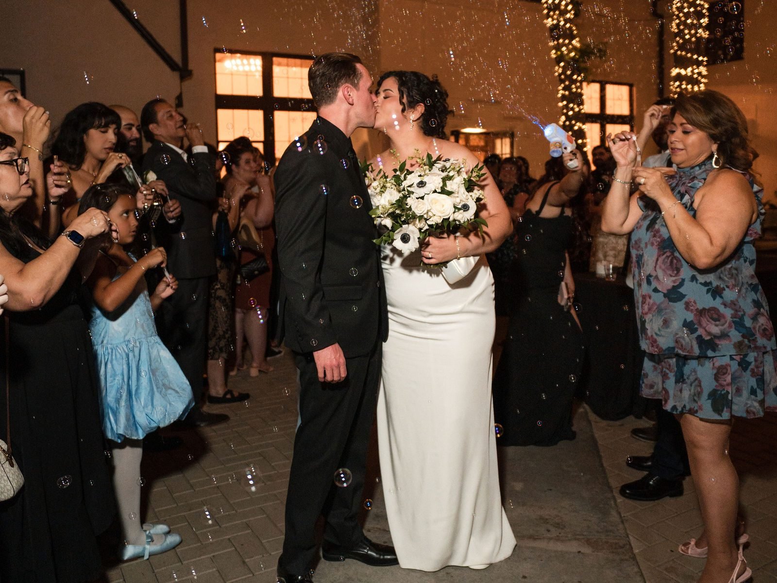 The couple walking out through their guests and a cloud of bubbles at night