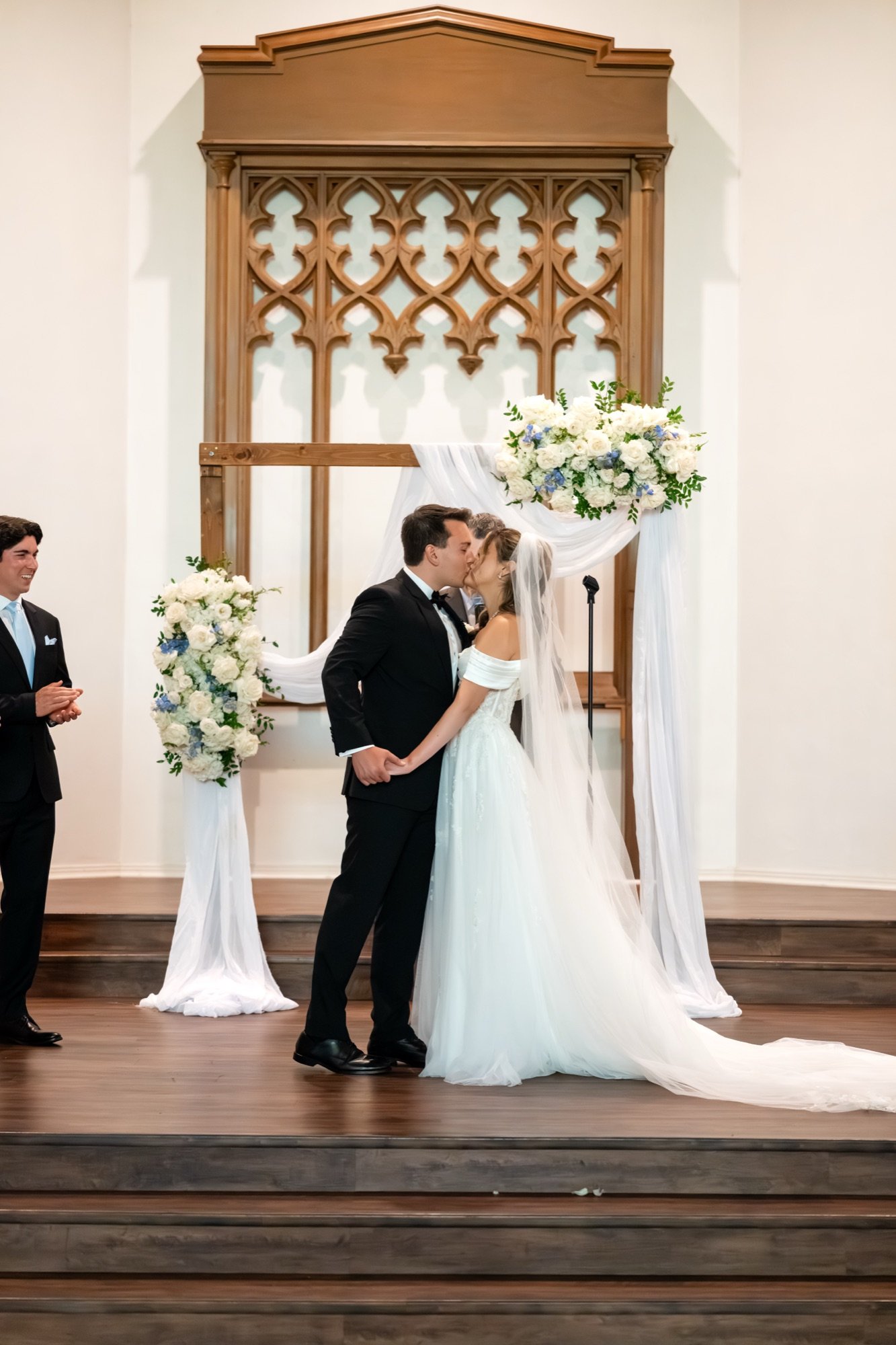 The couple kissing at the altar beneath carved wood screens and white flowers