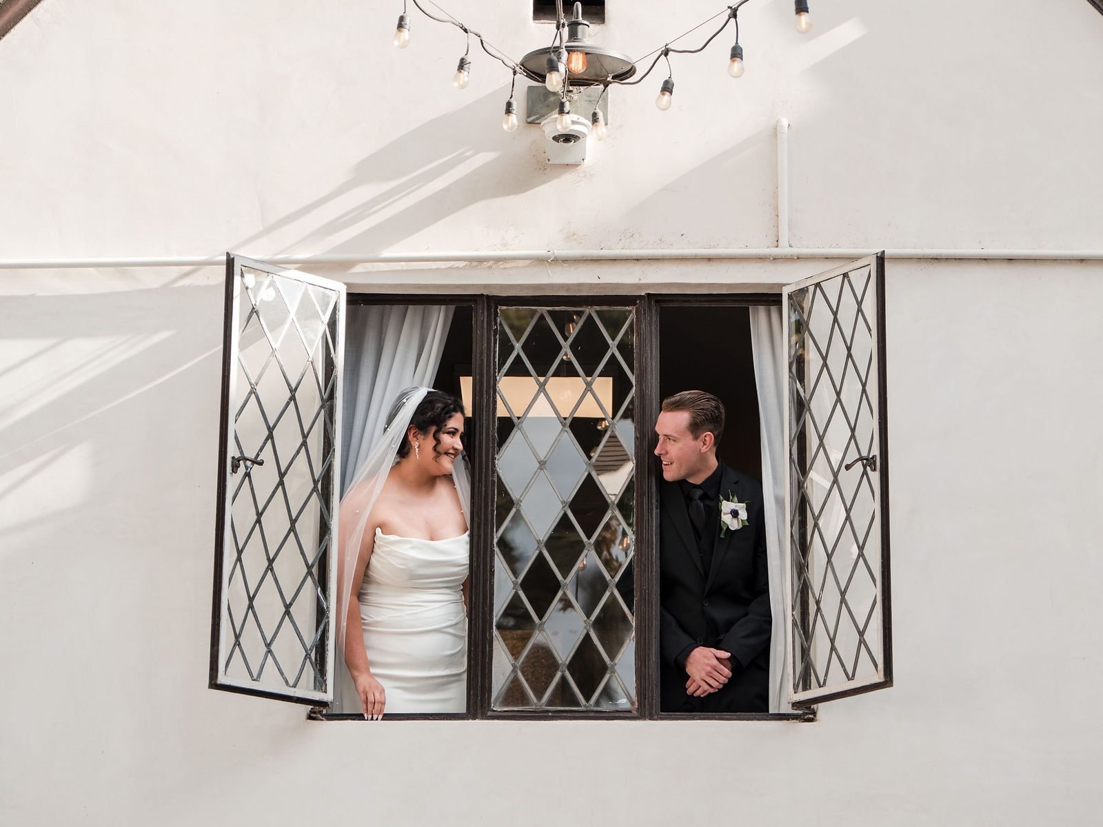 The couple leaning toward each other through a diamond-paned window on the white facade in daylight